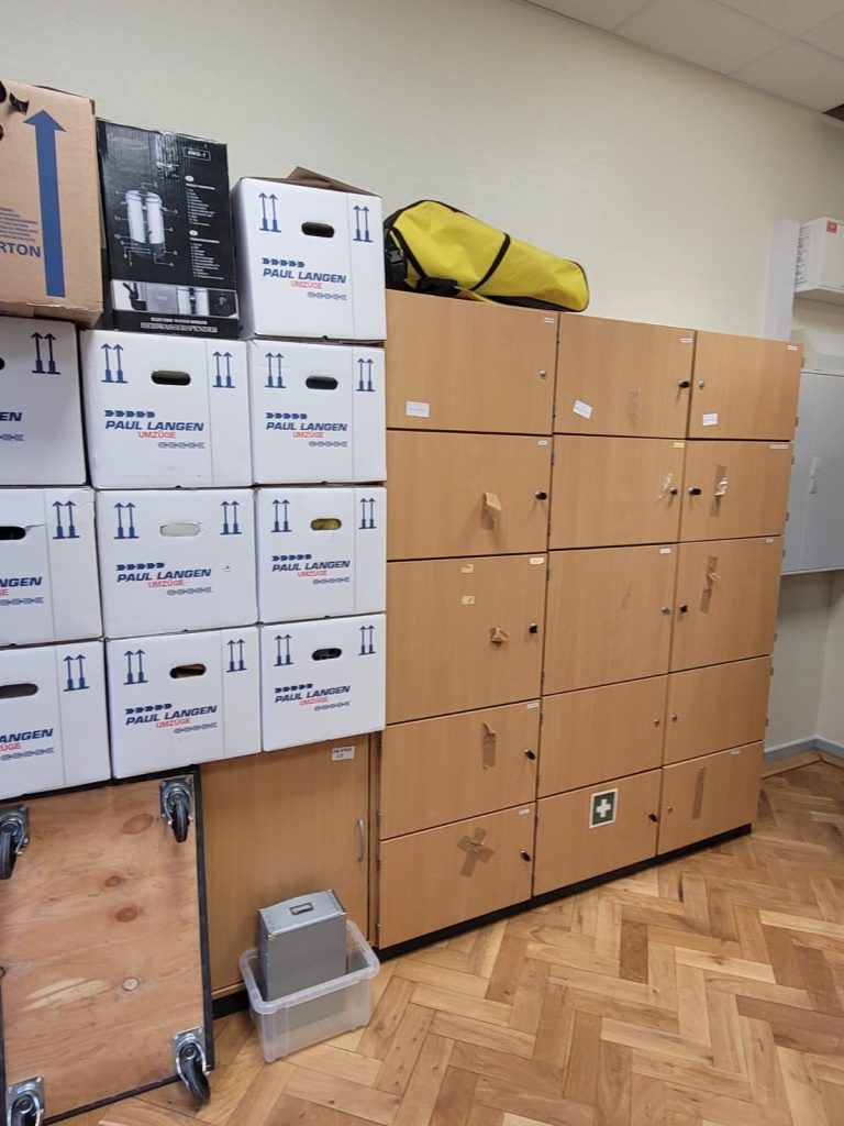Umzugskartons und Büroschränke in hellem Raum mit Parkettboden, gelbe Transporttasche auf Schrank