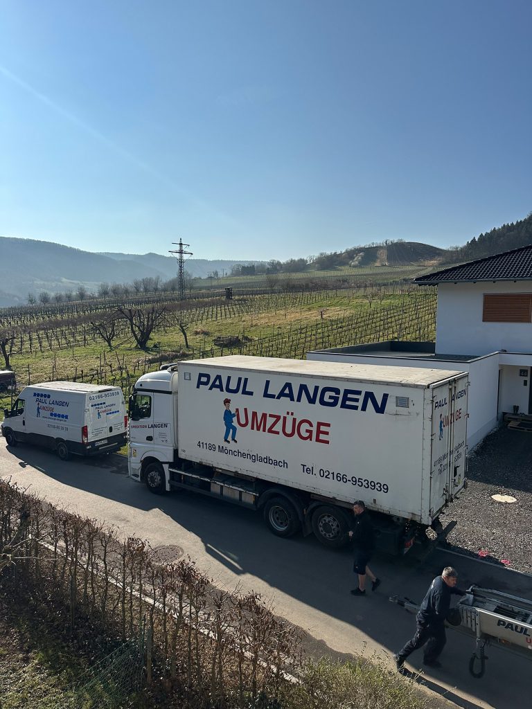 Paul Langen Umzugswagen vor Wohnhaus in ländlicher Weinbauregion mit Hügeln und Weinbergen im Hintergrund