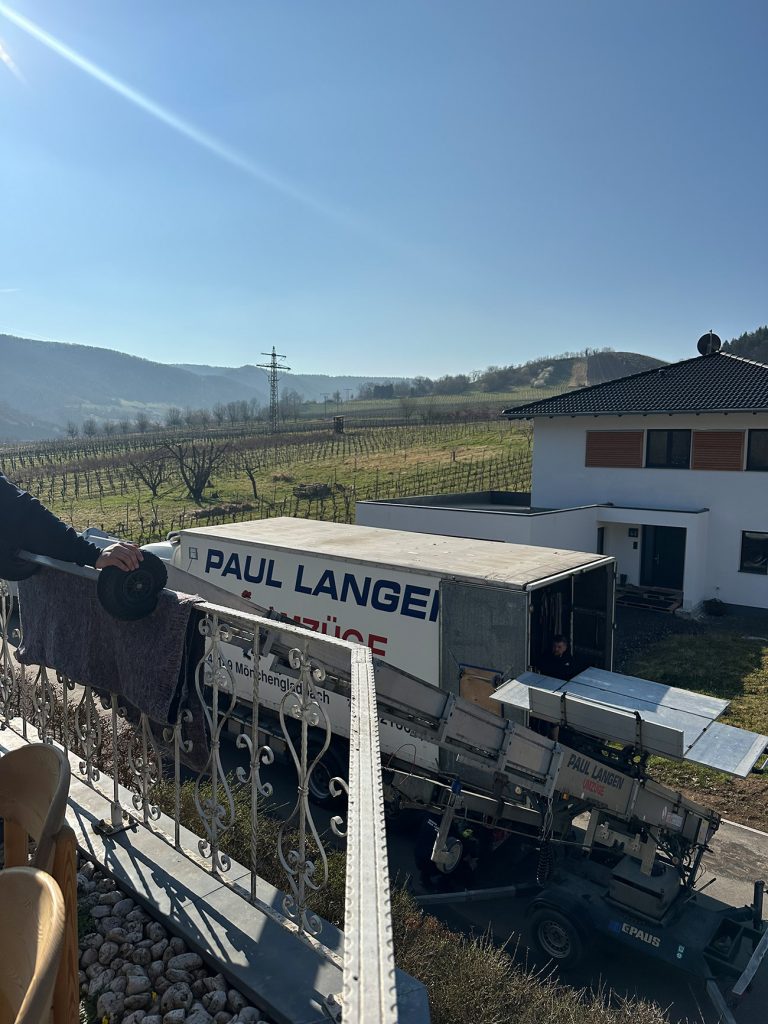 Paul Lange Umzugswagen vor modernem Einfamilienhaus in ländlicher Weinbauregion mit Hügeln im Hintergrund